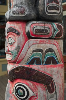 Skagway, AK, USA - June 25, 2024: Detail of a totem pole standing on a raised wooden sidewalk outside a tourist establlishment in Skagway. clipart