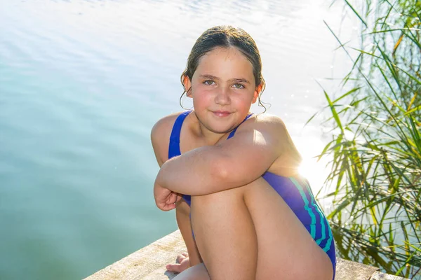 夏には 晴れた日には 川の近くのプラットフォームに水着の女の子が座っています — ストック写真