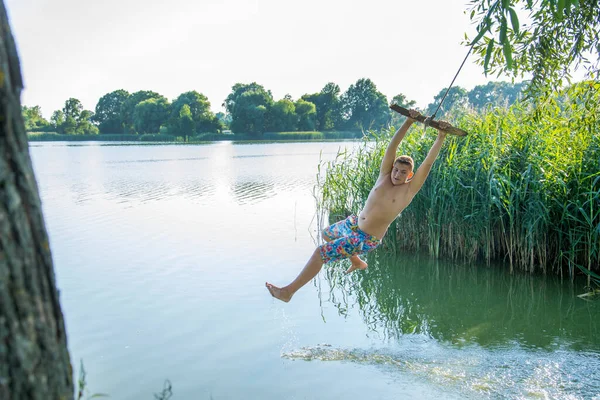 10代の男の子が面白いポーズでロープを振り 晴れた夏の日に水に飛び込む準備ができています — ストック写真