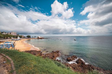 Salvador, Bahia - Brezilya - 24 Eylül 2024: Salvador 'da Porto da Barra plajı, renkli şemsiyelerle dolu kum, sakin denizde yıkanan ve arka planda Santa Maria Kalesi.