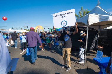 Los Angeles, Kaliforniya - ABD - 18 Ekim 2024: Seçmen kaydıyla ilgili bir tabela tutan adam, Los Angeles 'ta her yıl düzenlenen bir festival olan Taste of Soul sırasında, Afro-Amerikan kültürü ruh yemeği ve canlı müzikle kutlanır..