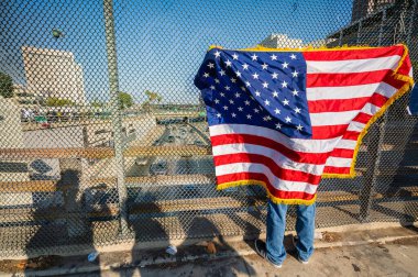 Los Angeles, ABD, 8 Haziran 2025: İCE operasyonlarının genişletilmesi ve göçmen haklarına destek gösterileri sırasında köprüde bir Amerikan bayrağı tutan protestocu