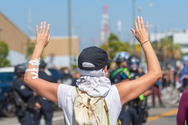 Los Angeles, ABD, 8 Haziran 2025: Genişletilmiş ICE operasyonlarına ve göçmen haklarına karşı düzenlenen gösteride protestocular ellerini kaldırarak polis memurlarının önünde diz çöktüler