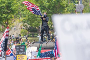 Los Angeles, California, ABD, 14 Temmuz 2025, Hükümet politikalarını protesto eden Krallar Yok sırasında otobüs durağının tepesindeki protestocu elinde bayraklar tutuyordu.