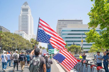 Los Angeles, Kaliforniya, ABD, 14 Temmuz 2025, Hükümet politikalarını protesto eden ve demokrasi ve göçmen haklarını destekleyen bir protestocu Amerikan bayrağını baş aşağı taşıyor.