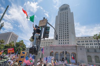 Los Angeles, California, ABD, 14 Temmuz 2025, Hükümet politikalarına karşı düzenlenen No Kings protestosu sırasında kadın Meksika bayrağıyla belediye binasının önündeki trafik ışıklarına tırmanıyor.