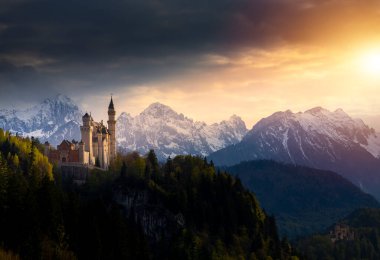 Gündoğumunda ünlü Neuschwanstein şatosu. Arka planda renkli Alpler manzarası var.