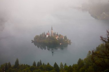 Bled Gölü 'ndeki adanın havadan görünüşü, arka planda Kanlı Şehir. Ada 'daki kilise ve diğer binalar su yüzeyine yansıyor..