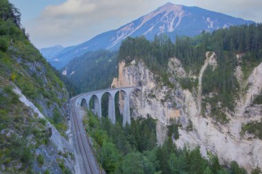A local train of Rhaetian Railway coming out of the tunnel in a cliff crossing famous Landwasser Viaduct over a deep gorge with fall colors on the rocky mountainside in Filisur, Grisons, Switzerland