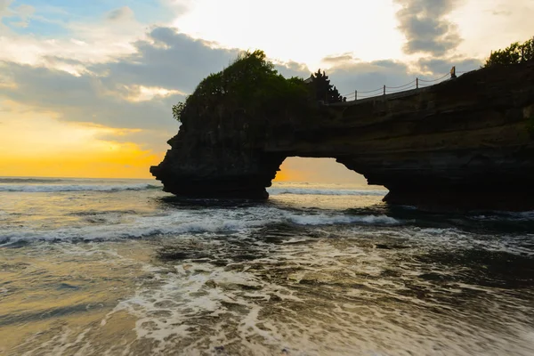 stock image Natural rock cave formation and wave in the sunset at Pura Batu Bolong, Indonesia