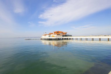 Sahilde bir rıhtım ve batık bir gemi, uzun pozlama tekniğiyle fotoğraflanmış.