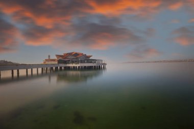 Sahilde bir rıhtım ve batık bir gemi, uzun pozlama tekniğiyle fotoğraflanmış.