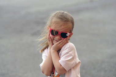 Dışarıda duran güneş gözlüklü küçük bir kızın portresi.