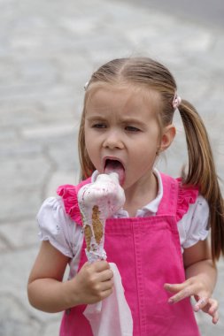 Kız sokakta dikilirken dondurma yiyor.