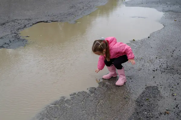 Şirin küçük kız yağmurdan sonra su birikintisine basmış. Lastik çizmeleri var ve çok mutlu.