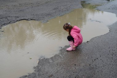 Şirin küçük kız yağmurdan sonra su birikintisine basmış. Lastik çizmeleri var ve çok mutlu.