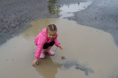 Şirin küçük kız yağmurdan sonra su birikintisine basmış. Lastik çizmeleri var ve çok mutlu.