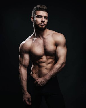 Siyah arka planda zayıf kaslı erkek model. Stüdyoda siyah pantalonlu üstsüz adam poz veriyor. Altı paket karın kası olan bir adam kameraya bakıyor..