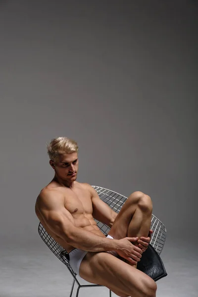 Sexy blond man in underwear. Muscled male model thinking and sitting on chair.