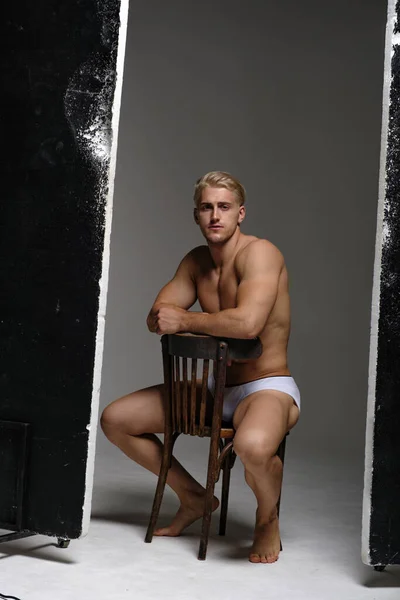 Sexy blond man in underwear. Muscled male model thinking and sitting on chair.