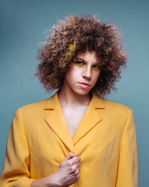 Curly fashion model in yellow jacket on blue background. Beautiful woman with curly hairstyling.