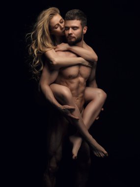 Siyah arka planda iki çıplak insan. Stüdyodaki yakışıklı çift. Güzel sarışın kız fitness erkek modeline biniyor..
