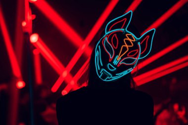 Illuminated Mystery: A vibrant figure shrouded in a glowing mask stands against a backdrop of pulsating red light beams, merging intrigue with electrifying energy. clipart