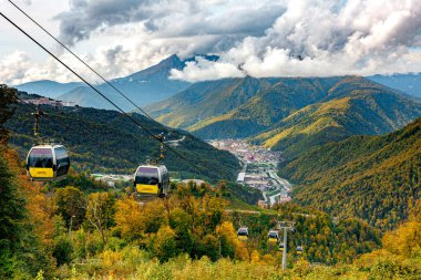 Whispers of Adventure Scenic Cable Cars Glide Above Serene Valley Town Nestled Amidst Majestic Mountains.! clipart