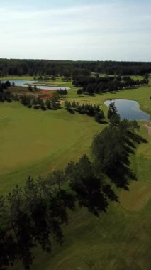 4K 'da Tranquil Water Bodies ve Verdant Trees tarafından çevrelenmiş Lush Golf Sahasının Çarpıcı Hava Görüntüsü 50 FPS ile. Huzurlu güzelliğin ve gökyüzünden geniş manzaraların tadını çıkar..