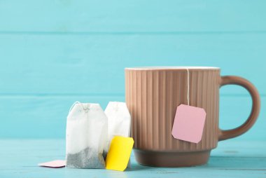 Mavi arka planda çay poşeti etiketli beyaz seramik bardak. Üst görünüm