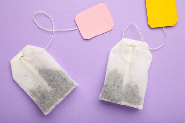 Mor arka planda etiketli çay poşetleri. Minimalizm, düz yatak, yazı için yer. Üst görünüm