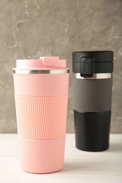 Two thermo cups or thermos mugs for tea or coffee on light background. Black and pink for him and her. Hot beverage for couples. Top view