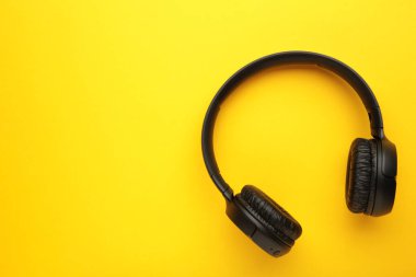 Black, modern wireless headphones on a yellow background. Top view.