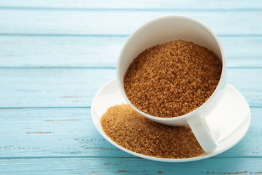 Brown sugar in white cup on blue background. Top view