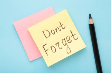 Reminder with text 'Don't forget' on a yellow memo on blue background. Top view