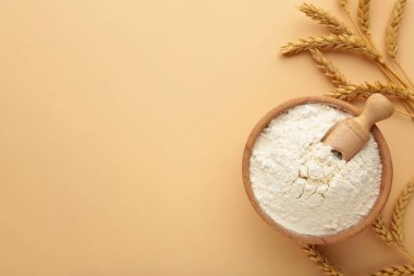 Wooden bowl with flour and flour spoon. Rice or wheat flour on beige background. top view