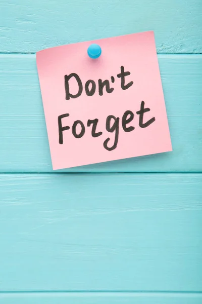 Reminder with text \'Don\'t forget\' on a pink memo on blue background. Top view.