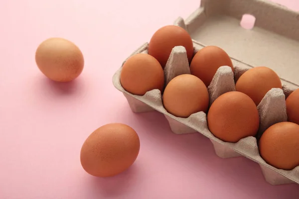 Chicken eggs in an open egg carton on pink. Natural healthy food and organic farming concept.
