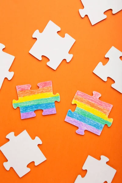 Concept LGBT as a part of society - two puzzle with the coloring of the flag of sexual minorities on orange background. Top view