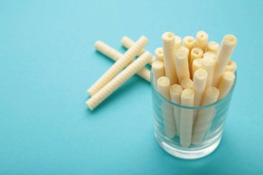 Delicious milk wafer rolls in glass on blue background. Top view