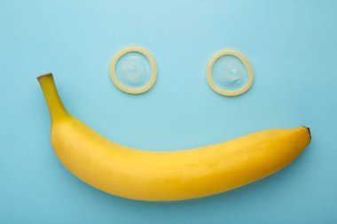Condom and banana on blue background with copy space. Top view
