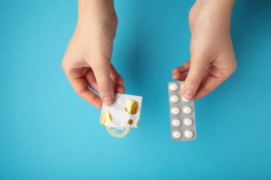 Contraceptive means: a condom and birth control pills in a hand on a blue background.