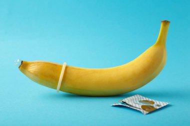 Condom and banana on blue background with copy space. Top view