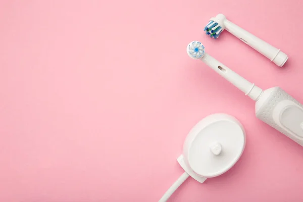 stock image Modern electric toothbrush with spare heads and charger on pink background. Space for text