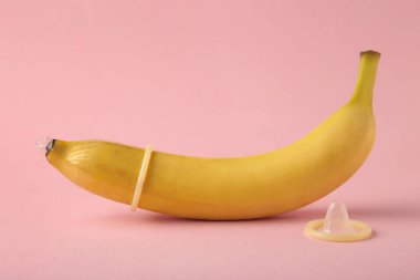 Condom and banana on pink background with copy space. Top view