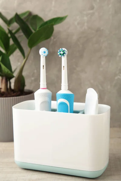 Halter Mit Modernen Elektrischen Zahnbürsten Und Pflanze Auf Blauem Hintergrund — Stockfoto