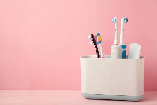 Holder with modern electric toothbrushes and manual toothbrushes on pink background. Space for text