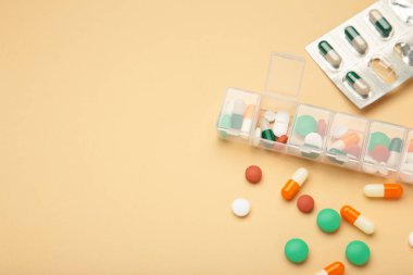 Günlük ilaç kutusu ve bej arka planda besin takviyeleri. Üst görünüm