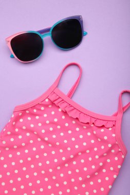 Yaz çocuğunun tatil konsepti. Mor arka planda şirin güneş gözlüklü mayo. Tatil konsepti, moda çocuğu. Üst görünüm