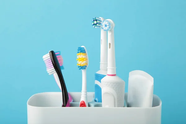 Holder with modern electric toothbrushes and manual toothbrushes on blue background. Space for text